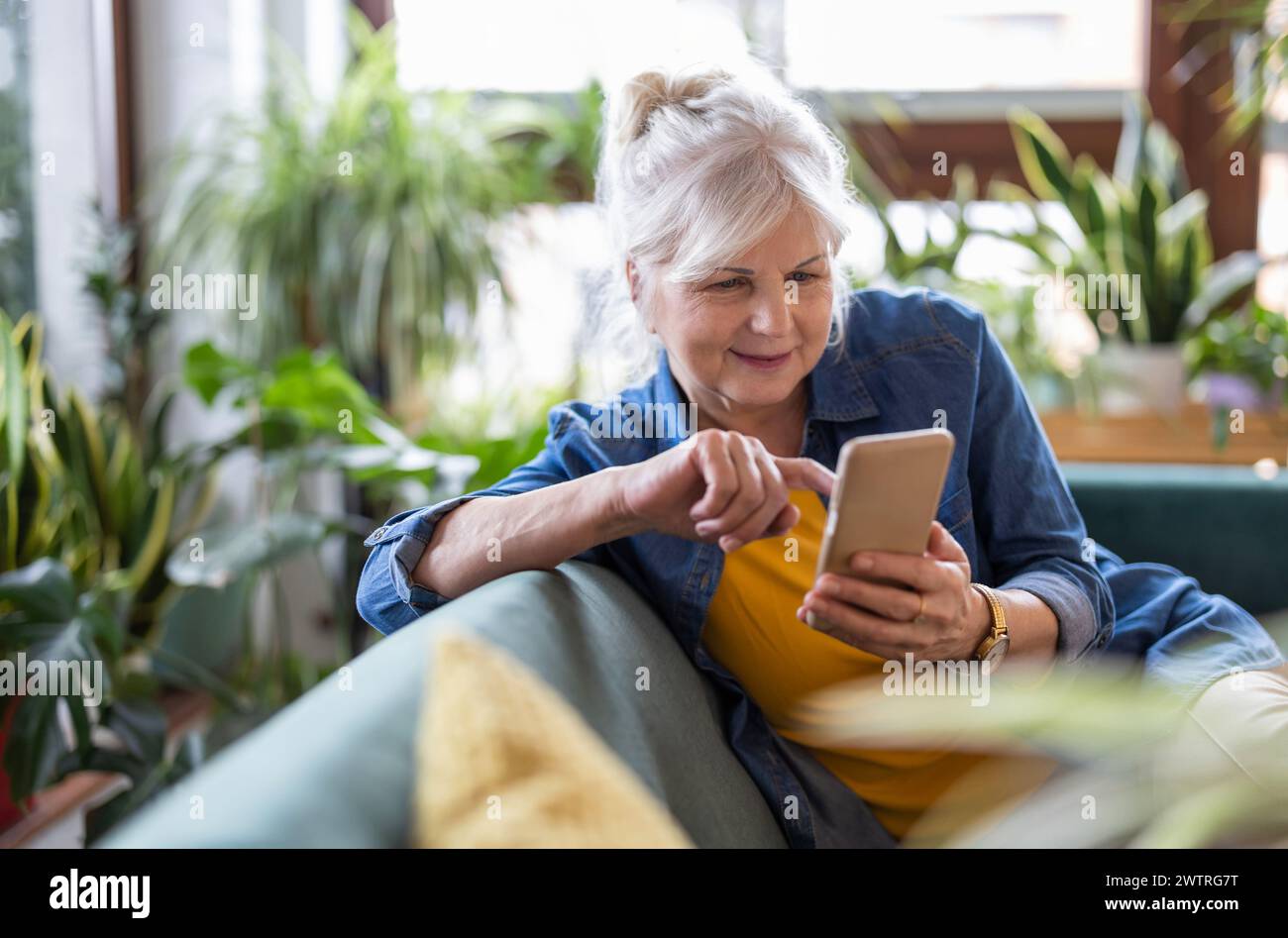 Smiling senior woman using smart phone while sitting on sofa at home Stock Photo