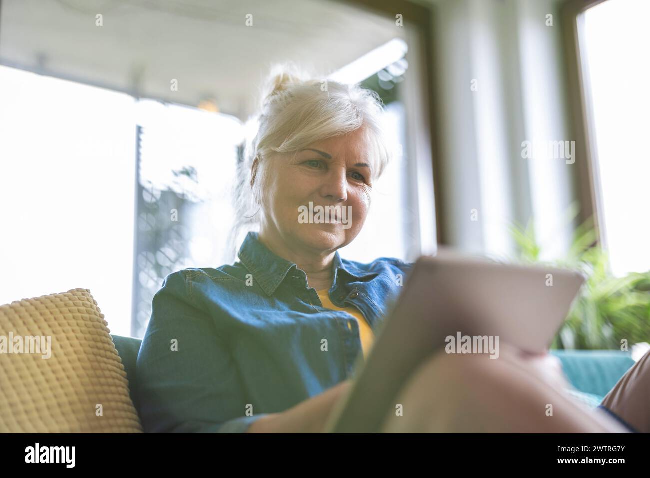 Mature woman using digital tablet while sitting on sofa at home Stock Photo