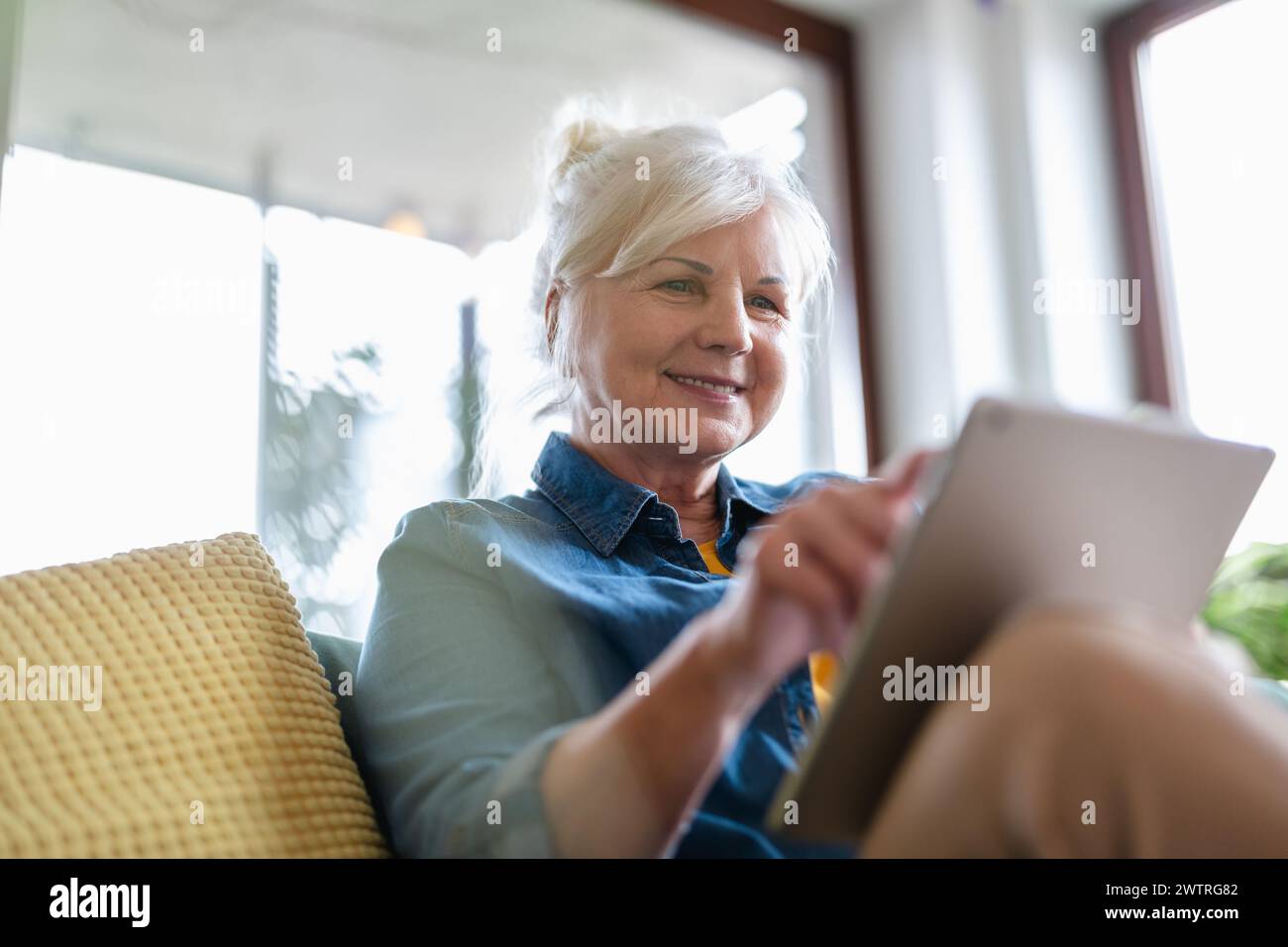 Mature woman using digital tablet while sitting on sofa at home Stock Photo