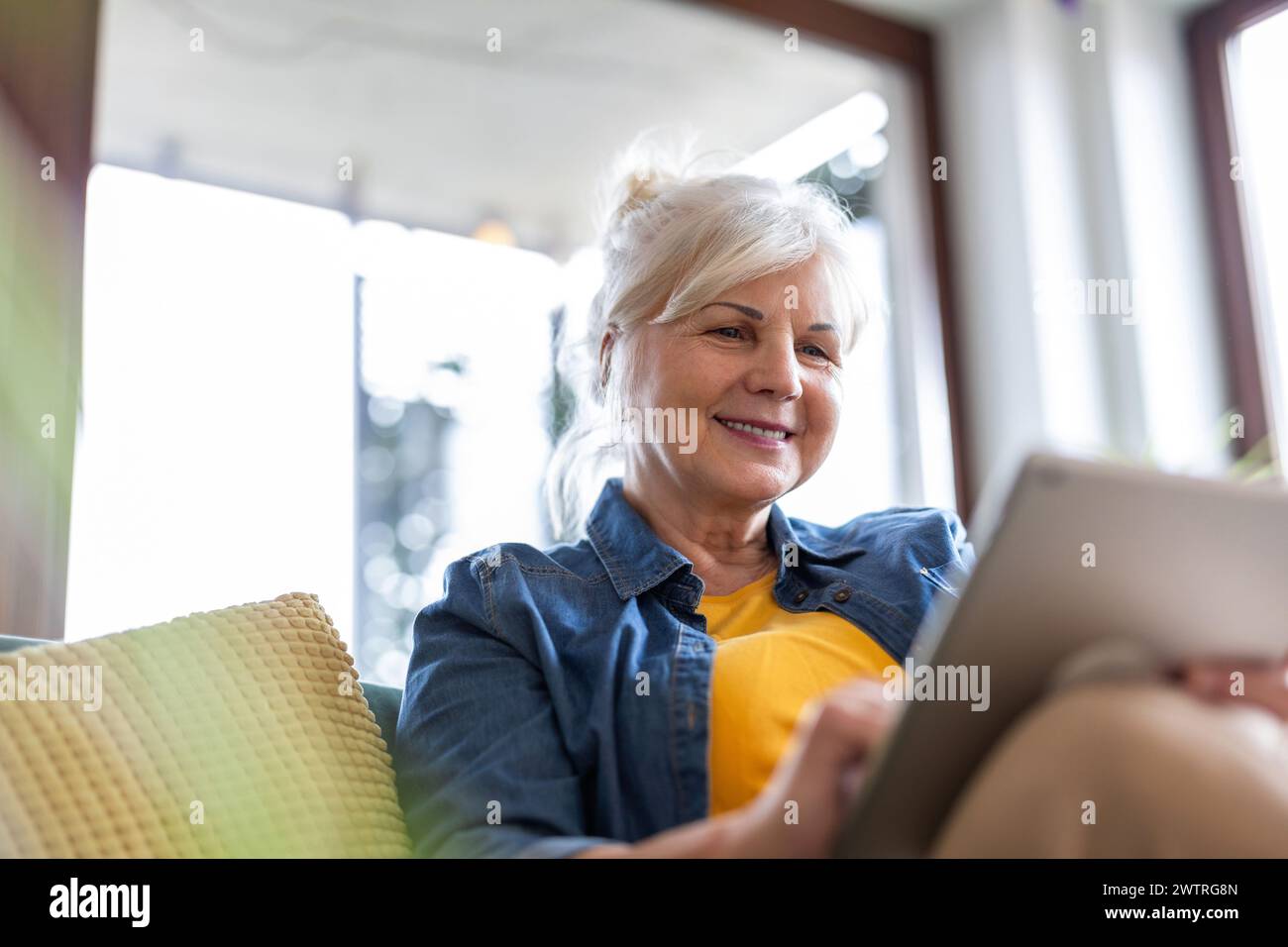 Mature woman using digital tablet while sitting on sofa at home Stock Photo