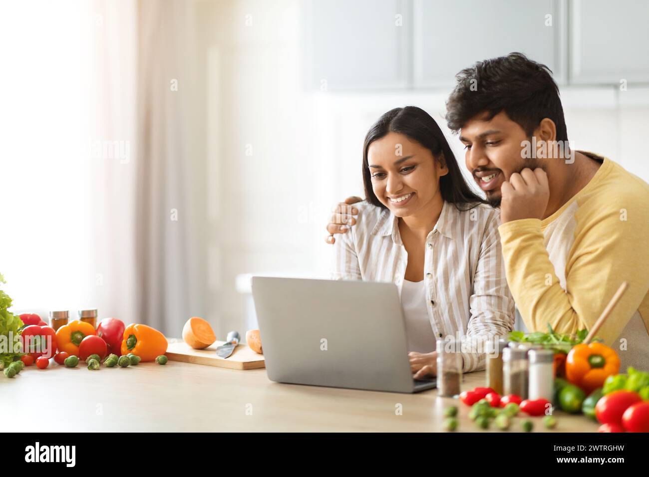 Happy loving young indian spouses using laptop while cooking Stock Photo