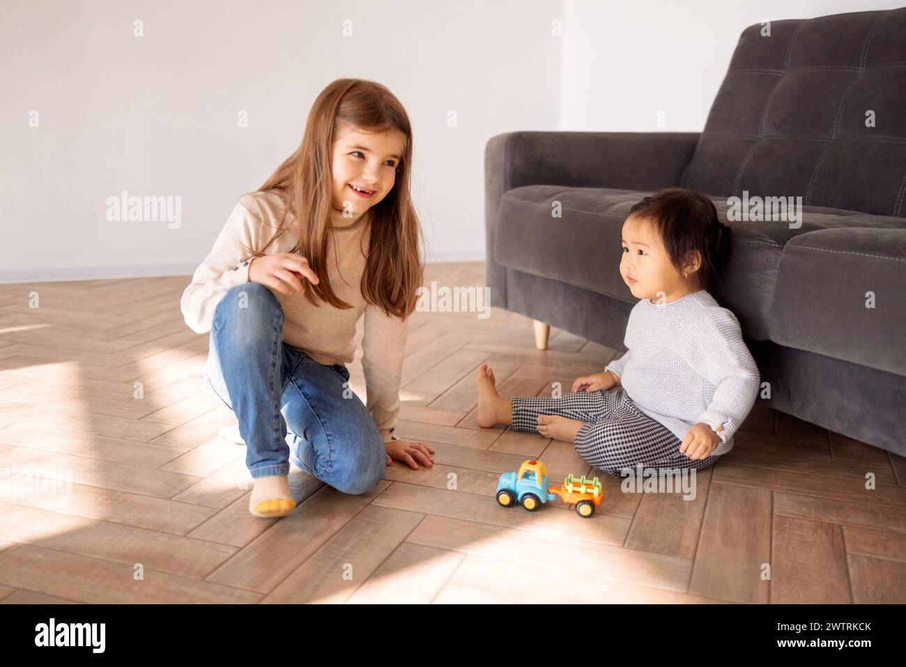 Little girls of different races sit and play in the living room of the house. Cute different multiethnic children have fun together on the floor at ho Stock Photo