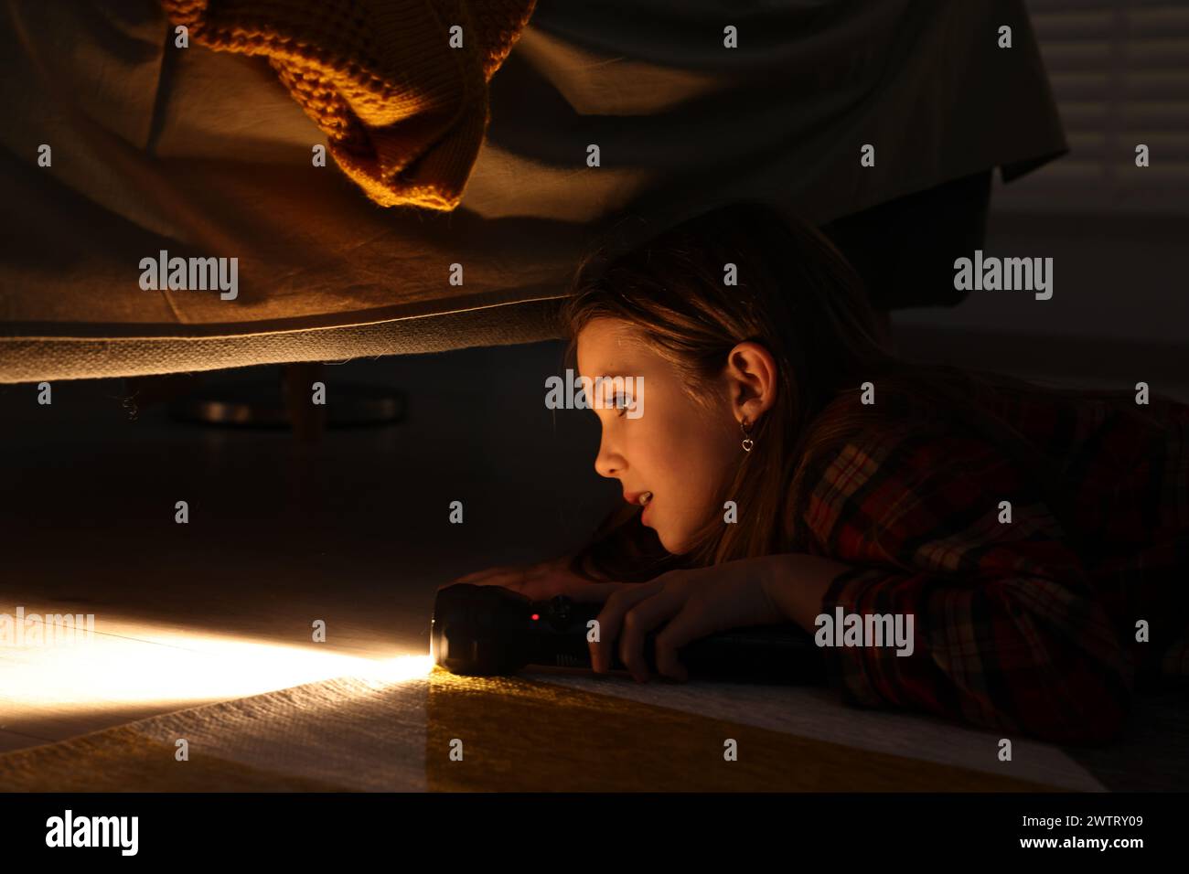 Little girl with flashlight looking for monster under bed at night Stock Photo