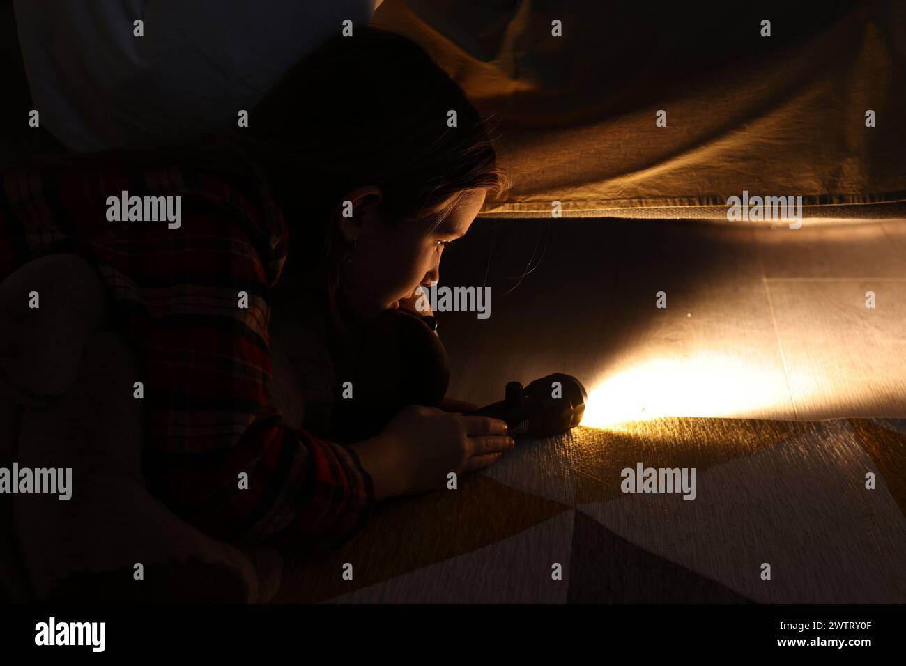 Little girl with flashlight looking for monster under bed at night Stock Photo