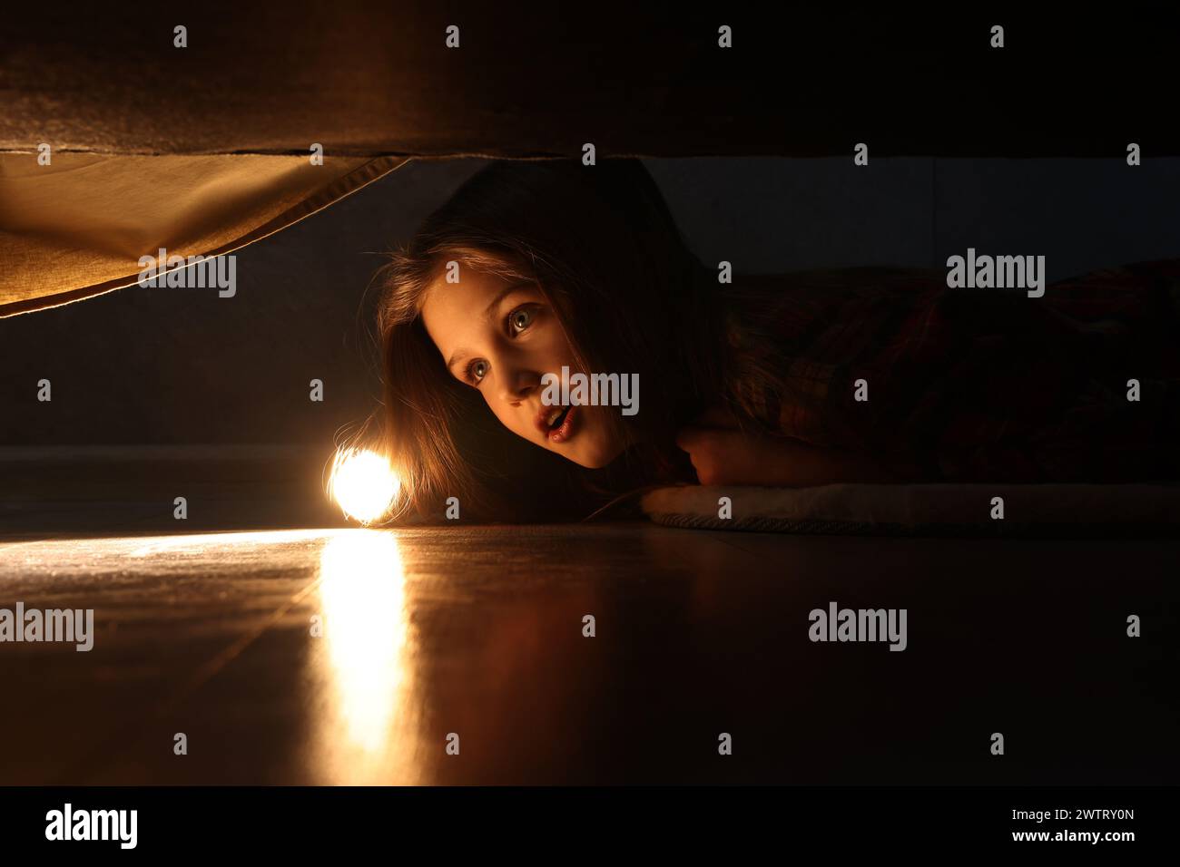 Little girl with flashlight looking for monster under bed at night Stock Photo