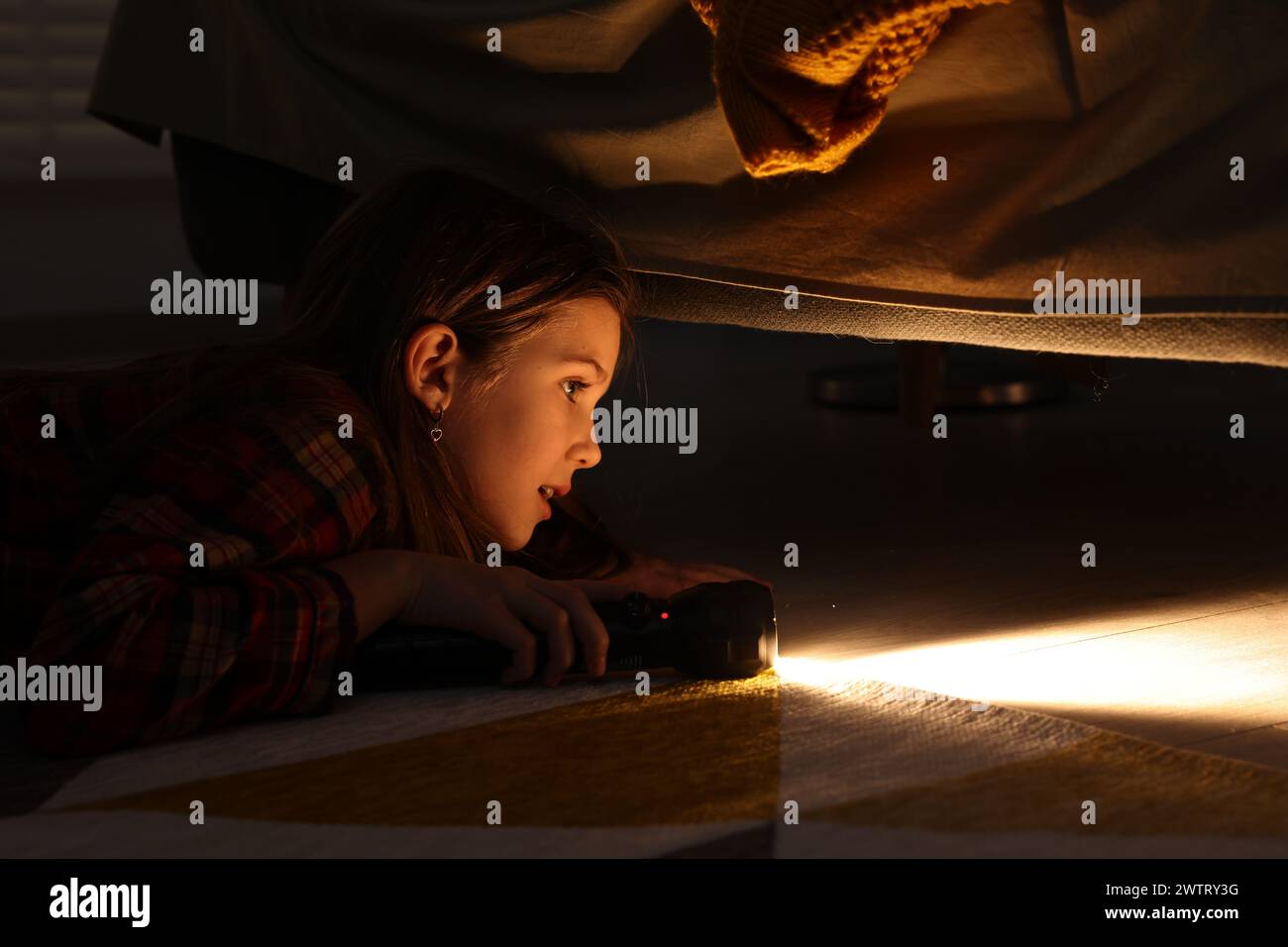 Little girl with flashlight looking for monster under bed at night Stock Photo