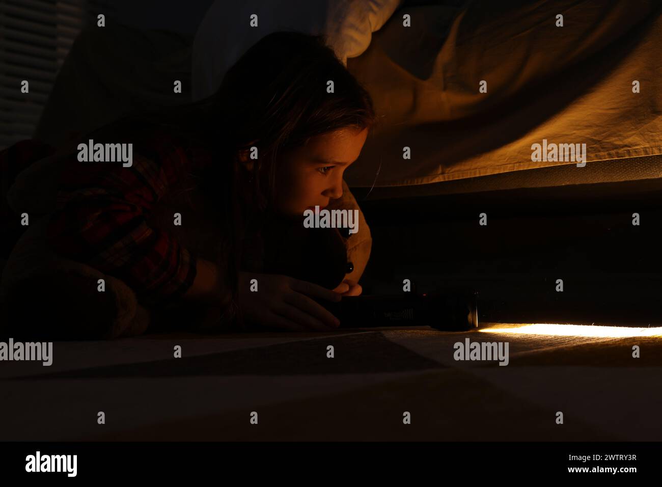 Little girl with flashlight looking for monster under bed at night Stock Photo