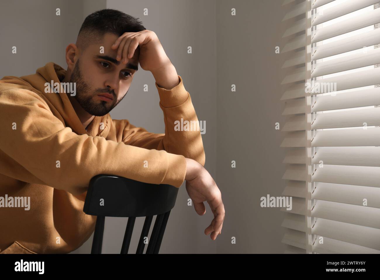 Sad man sitting on chair near window. Space for text Stock Photo