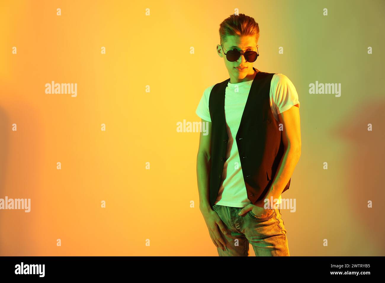 Stylish young man in sunglasses on color background in neon lights ...