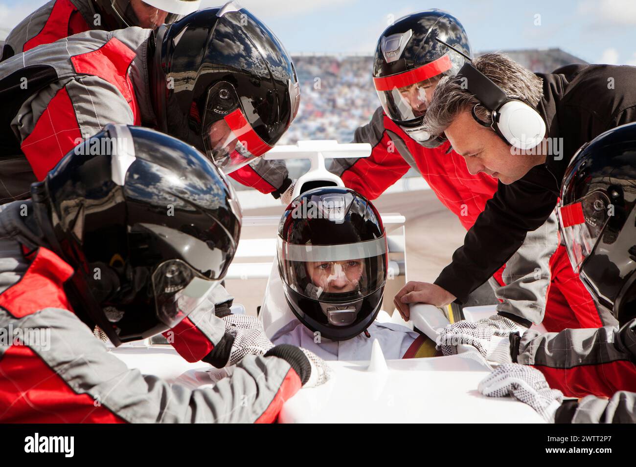 Race car driver getting ready for a big race with the pit crew team huddled around. Stock Photo