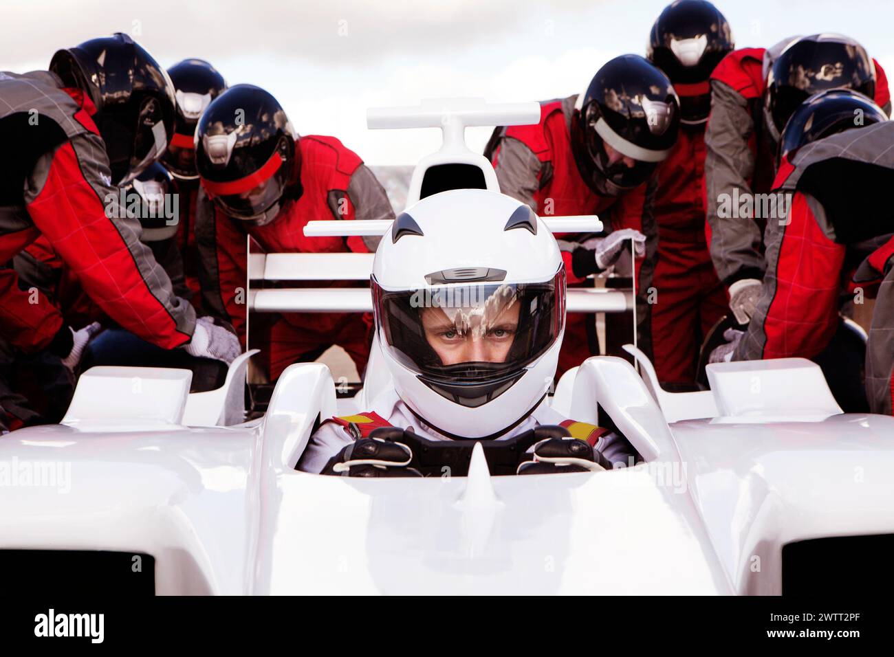 Race car driver focused at the starting line with a pit crew ready for action. Stock Photo