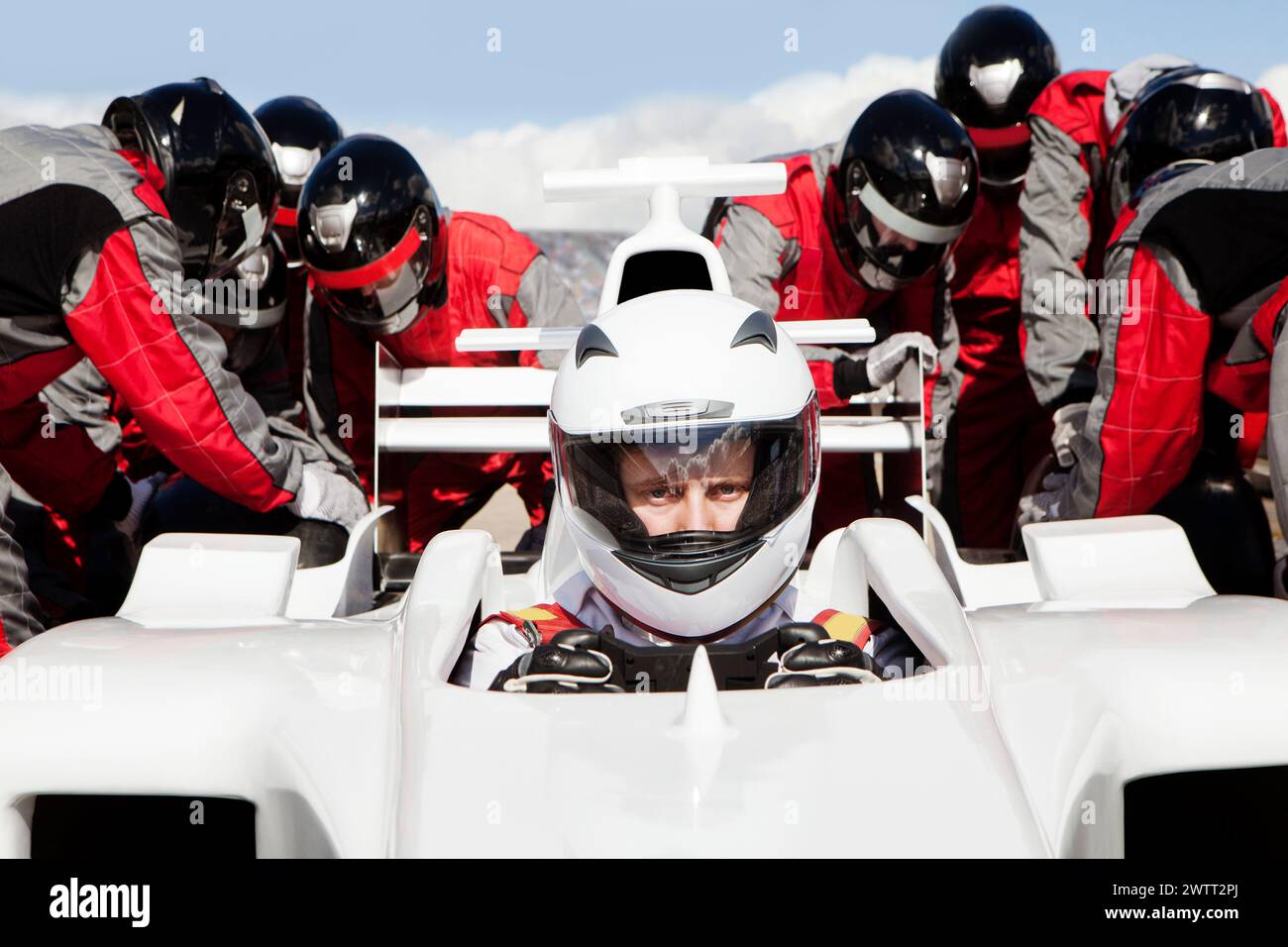 Focused race car driver at the starting line with pit crew team ready for action Stock Photo