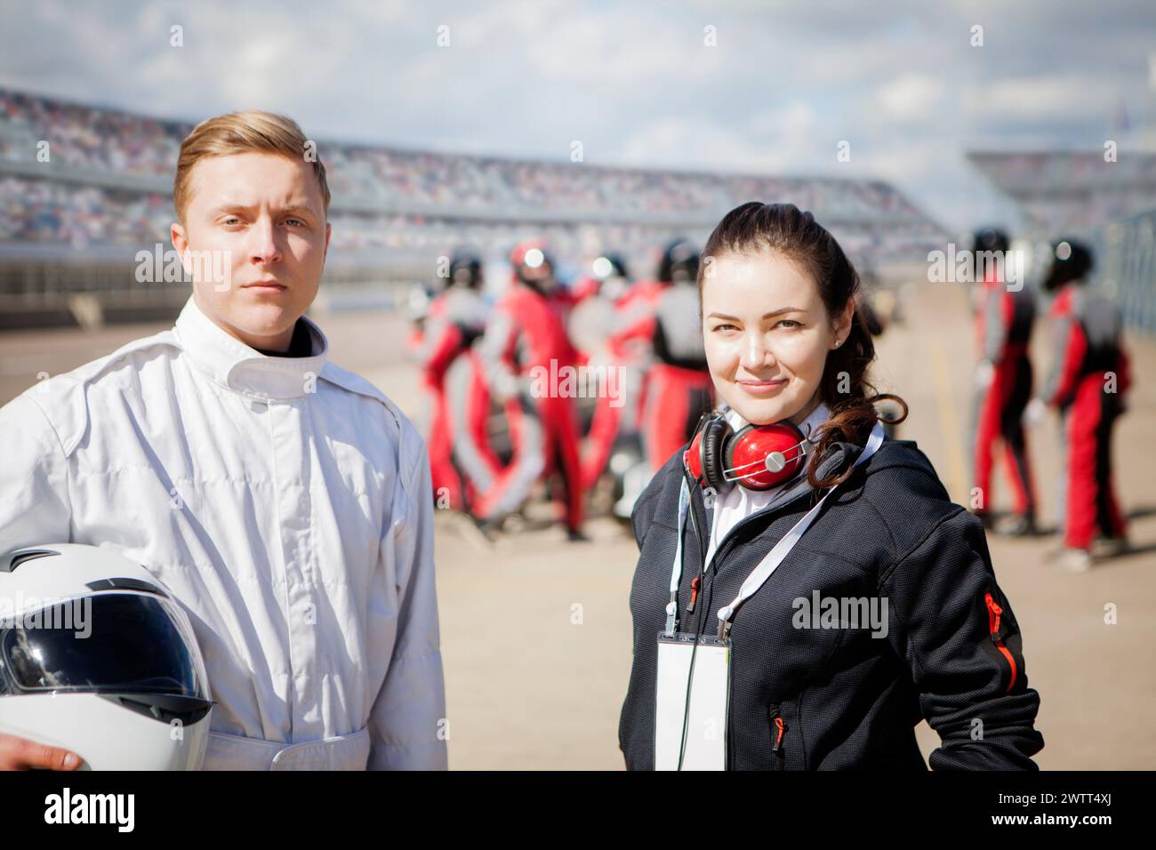 Racing team members poised confidently at the racetrack with pit crew in the background. Stock Photo