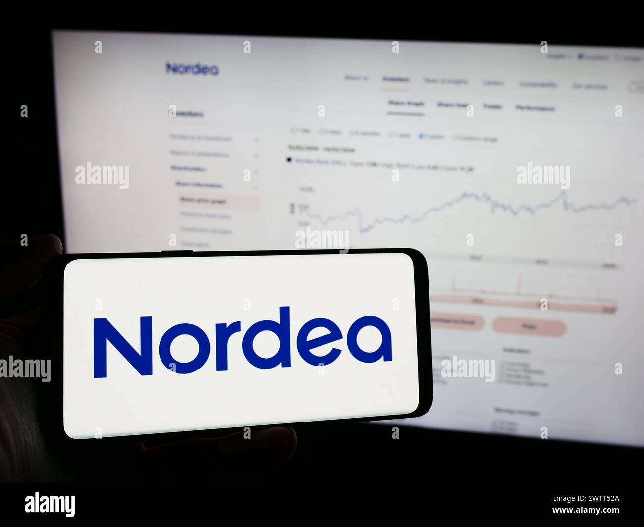 Person holding mobile phone with logo of Finnish financial services company Nordea Bank Abp in front of business web page. Focus on phone display. Stock Photo