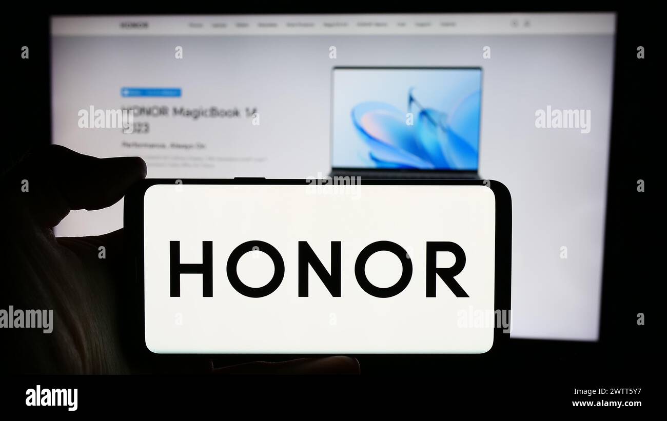 Person holding cellphone with logo of Chinese smartphone company Honor Device Co. Ltd. in front of business webpage. Focus on phone display. Stock Photo