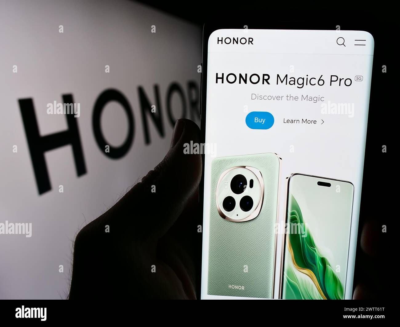 Person holding cellphone with webpage of Chinese smartphone company Honor Device Co. Ltd. in front of logo. Focus on center of phone display. Stock Photo