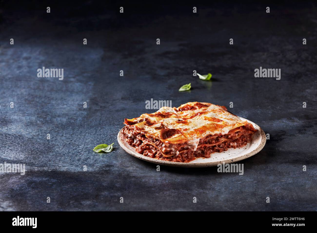A scrumptious slice of lasagna with fresh basil on a dark, rustic background. Stock Photo