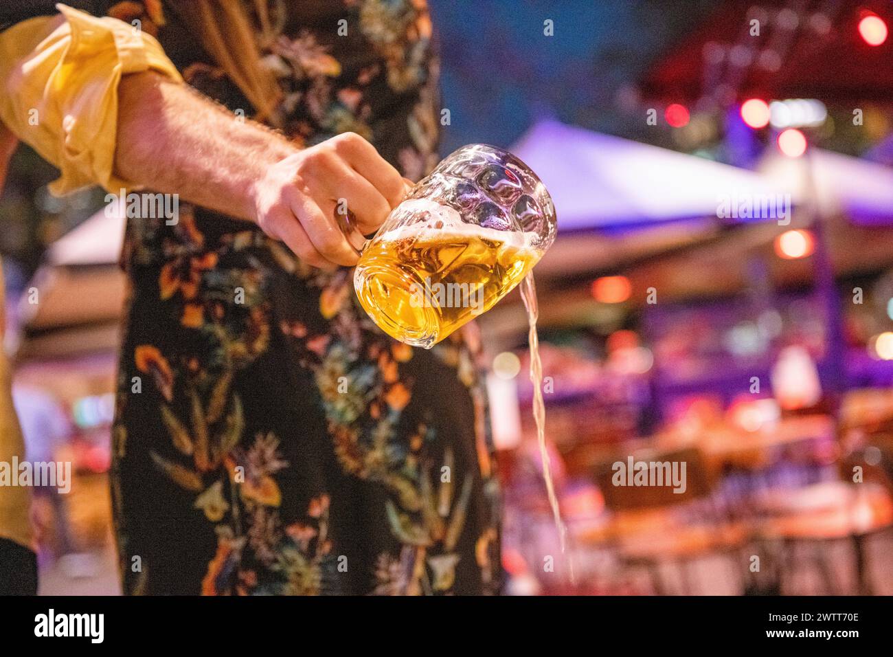 A person pouring a glass of beer with a dynamic splash against a lively bar backdrop. Stock Photo