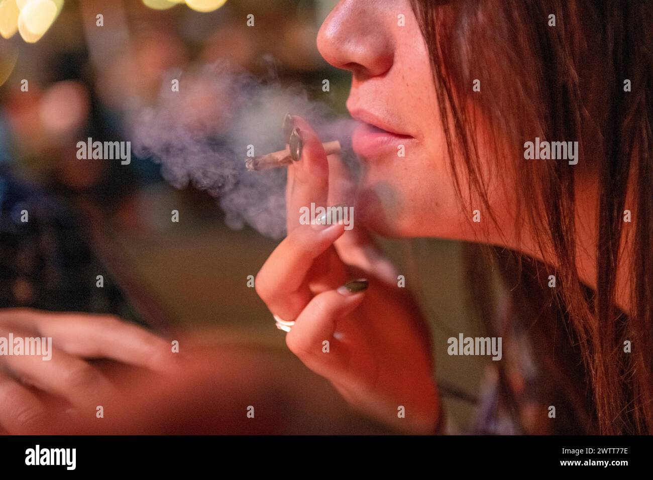 A young woman exhaling smoke from a lit cigarette at night. Stock Photo