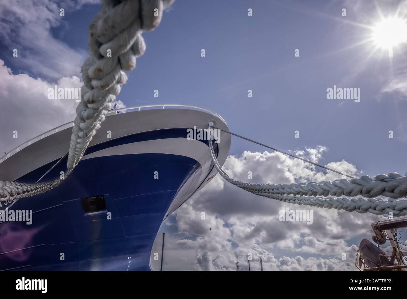 A ship moored under a sunny sky, viewed through the sturdy ropes that secure it Stock Photo