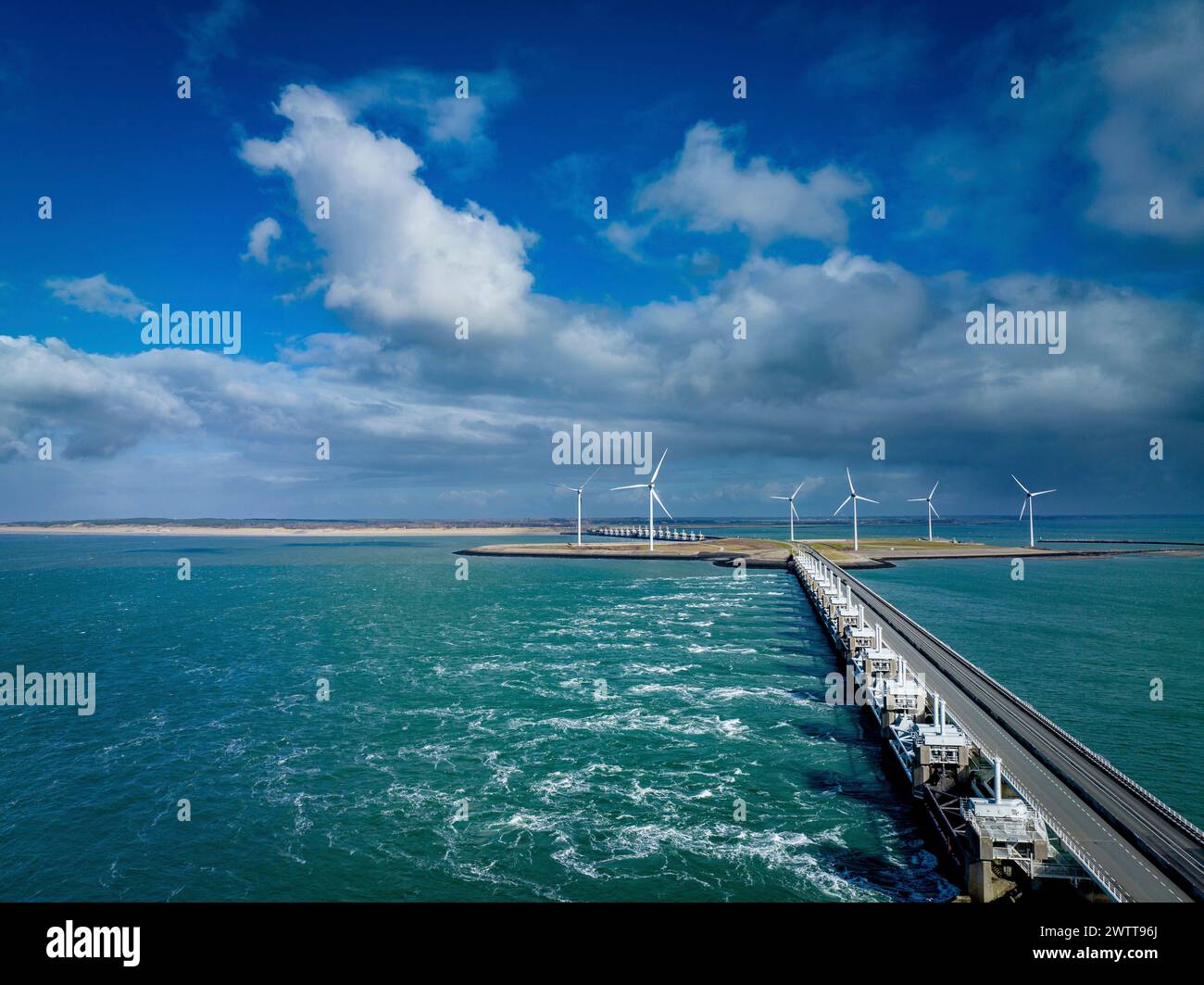 A scenic view of a pier leading to a wind farm on the coast under a bright blue sky. Stock Photo