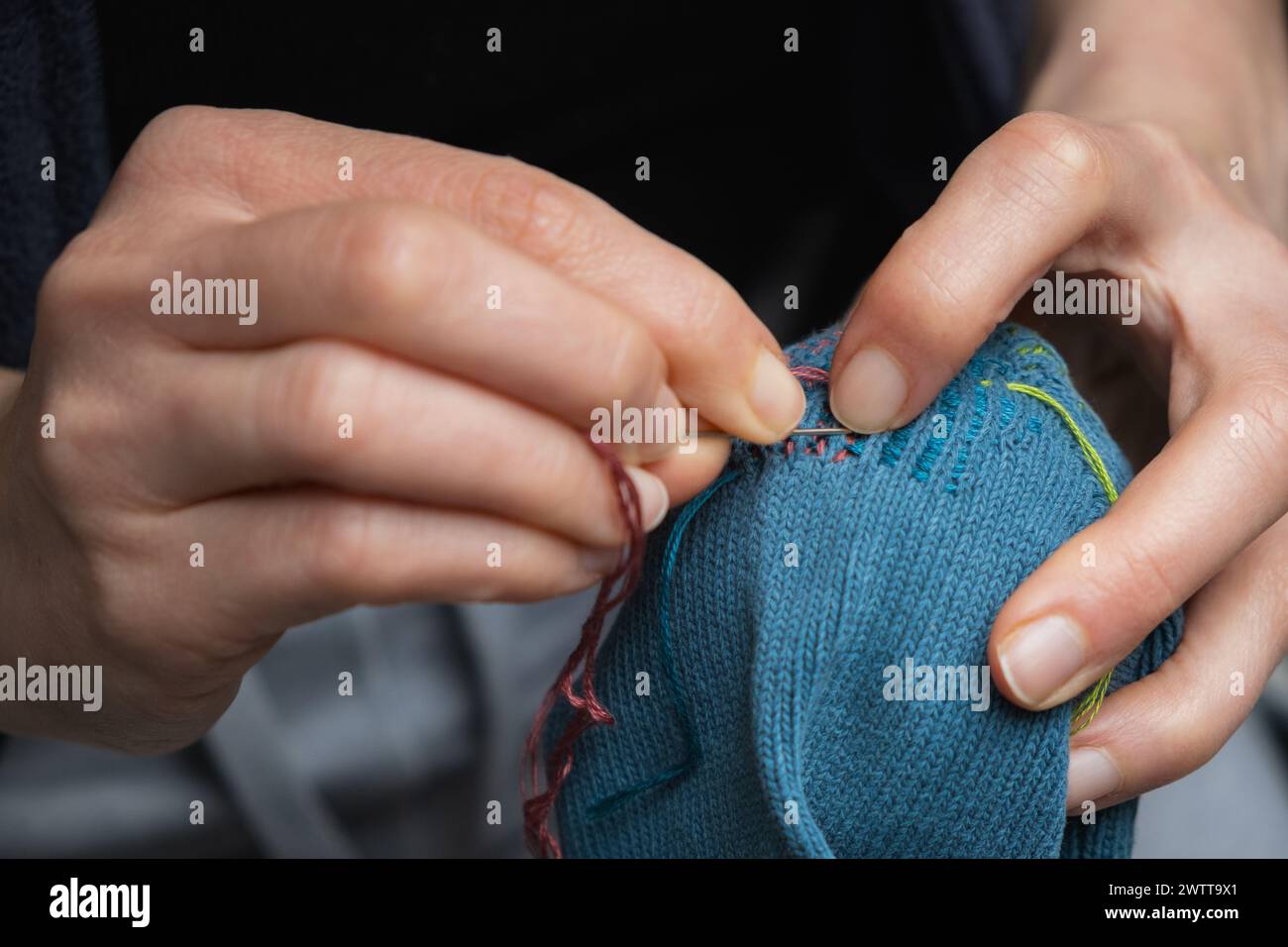Mending clothes. Visible mending repairing sock. Darning old socks, reducing waste, slow fashion. Repair concept, selective focus. Stock Photo
