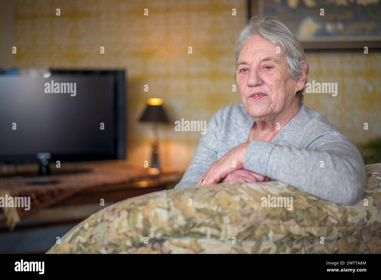 Elderly woman relaxing at home with a warm, contented smile. Stock Photo