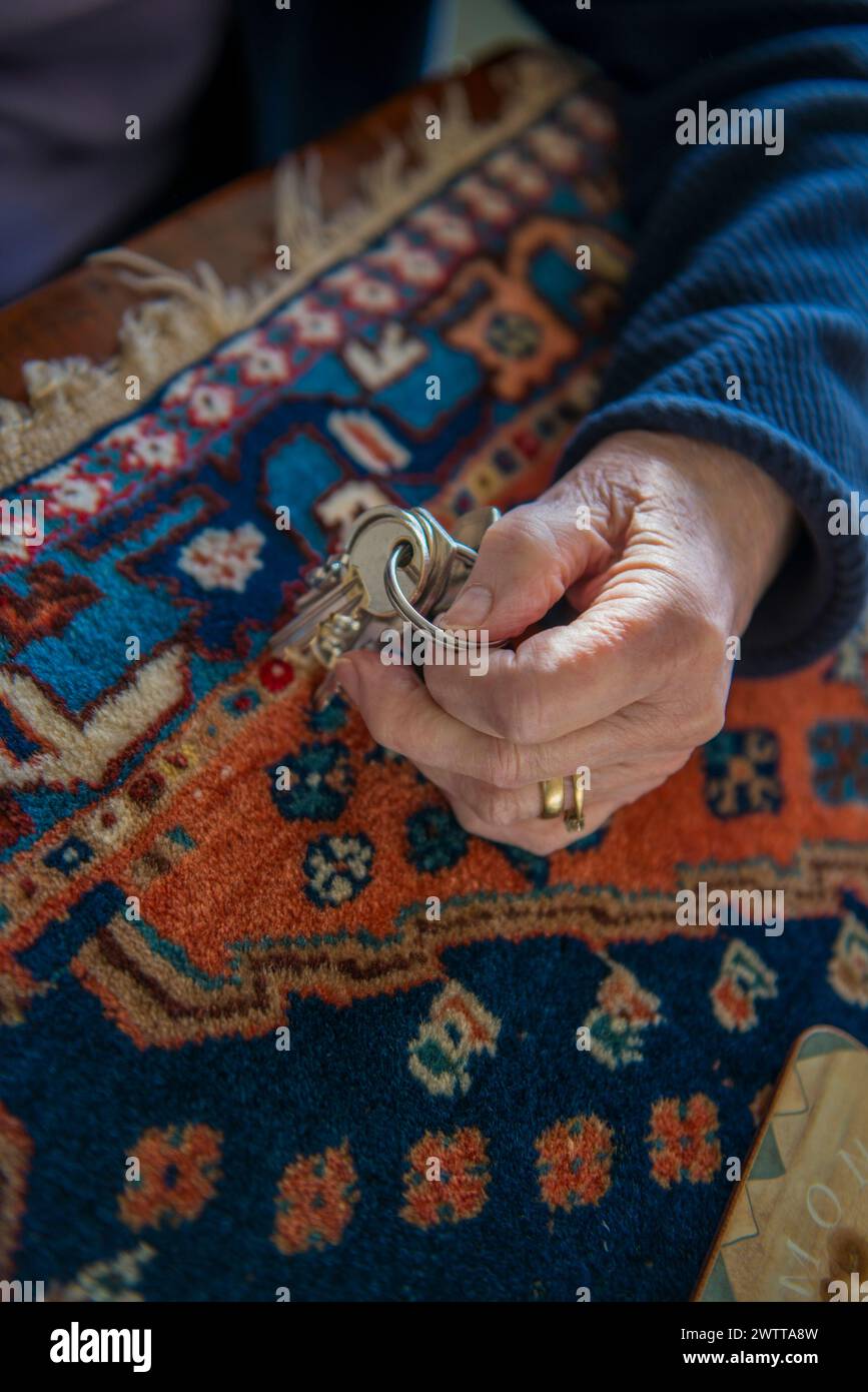 Elderly hands holding a key over a colorful patterned carpet. Stock Photo