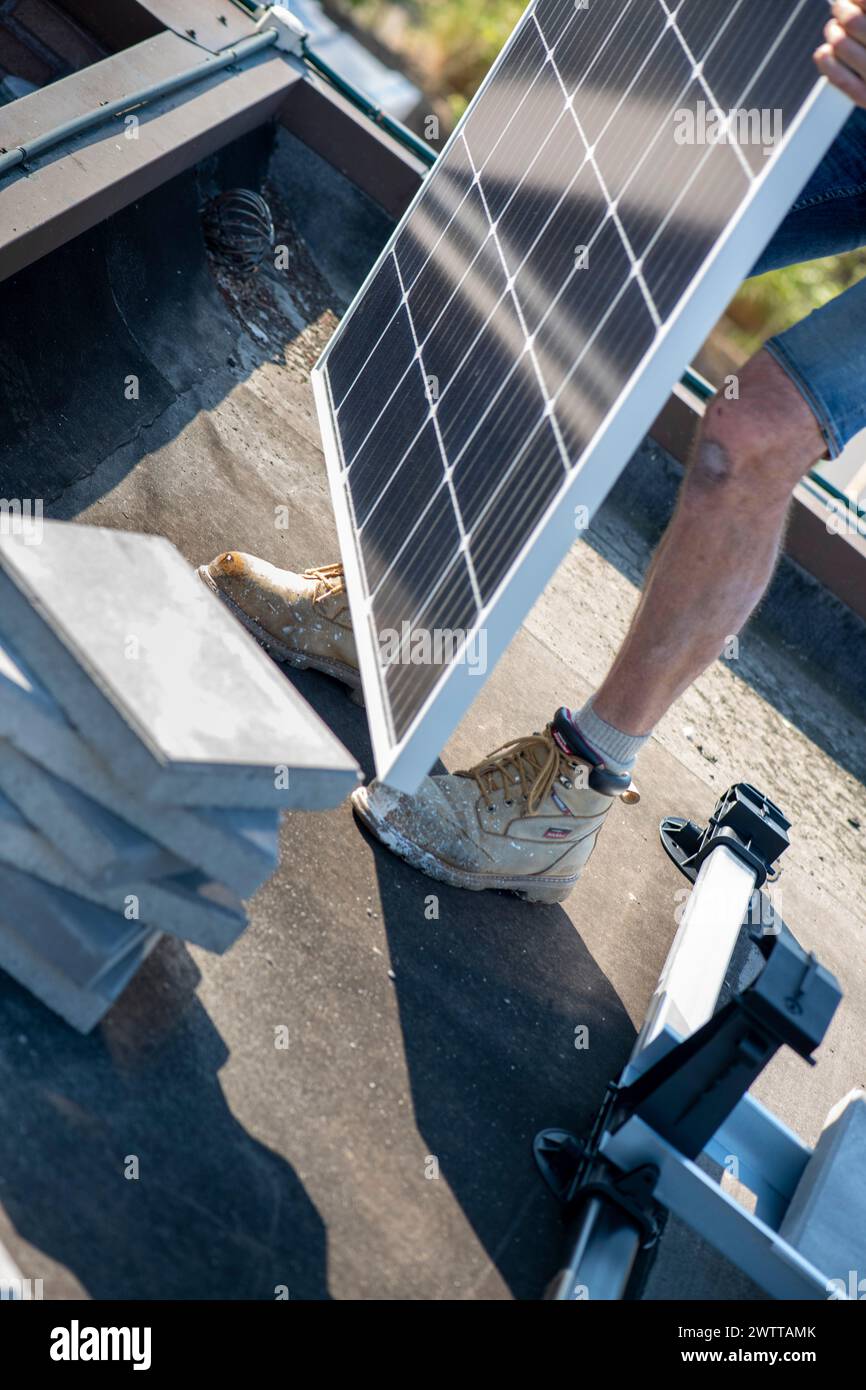 Worker installing a solar panel on a rooftop Stock Photo
