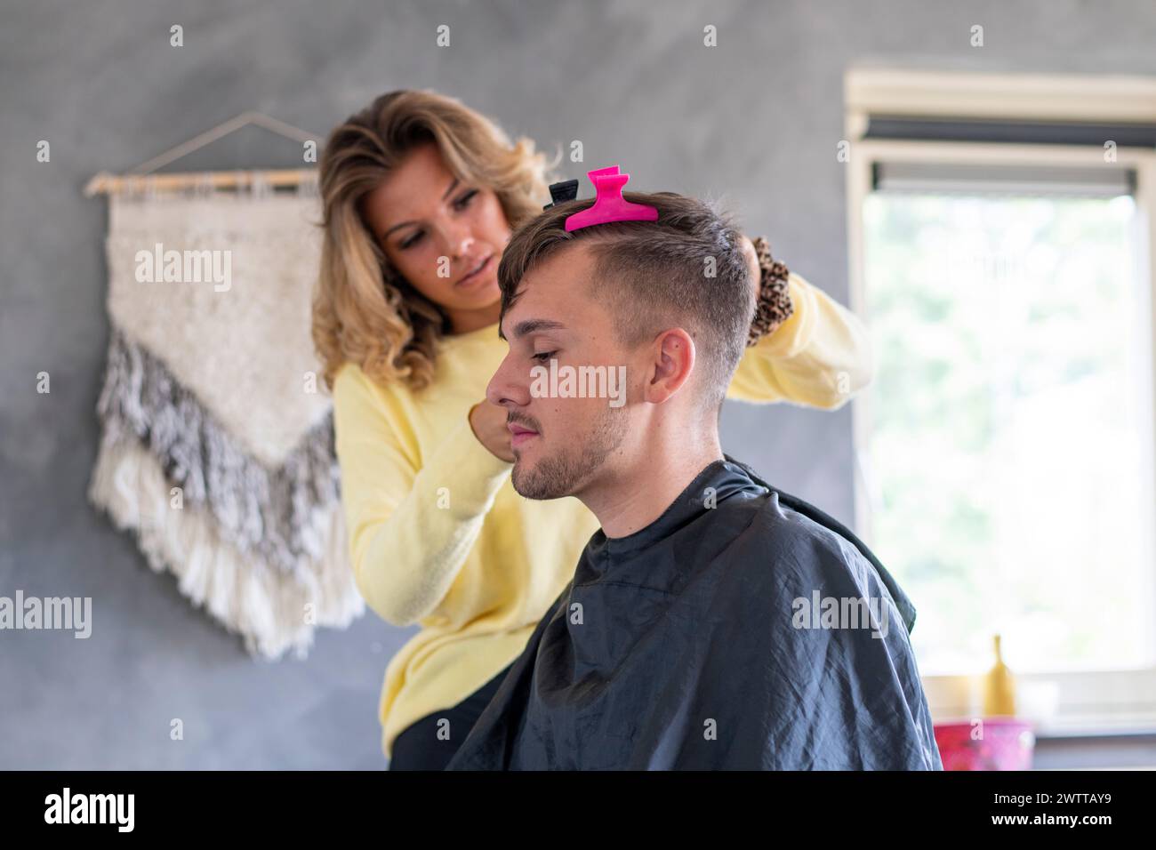 Hair stylist giving a new haircut to a male client in a cozy home setup. Stock Photo