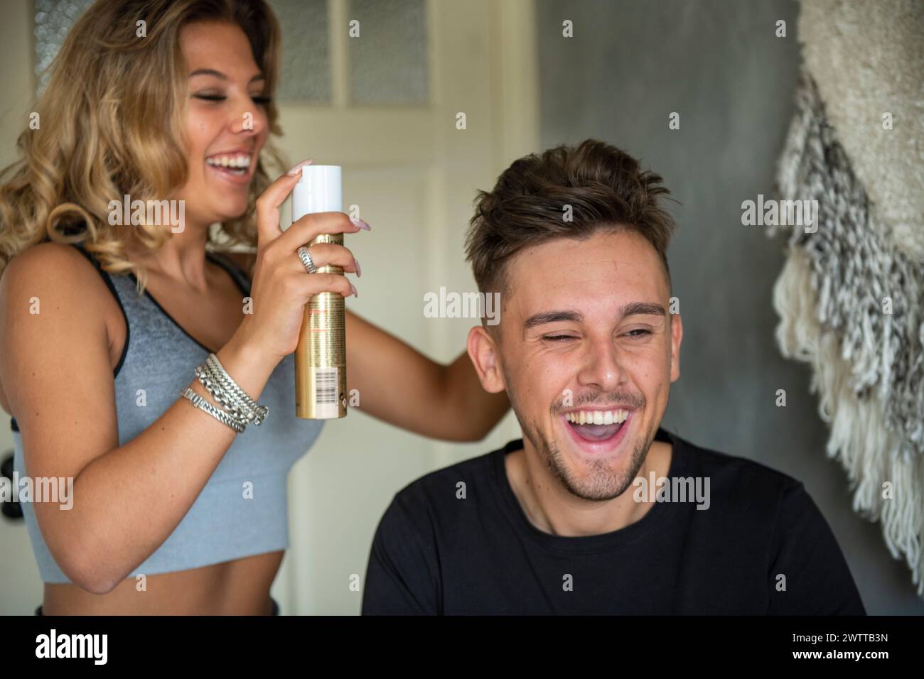 Woman styling man's hair with hairspray, both laughing in a candid moment. Stock Photo