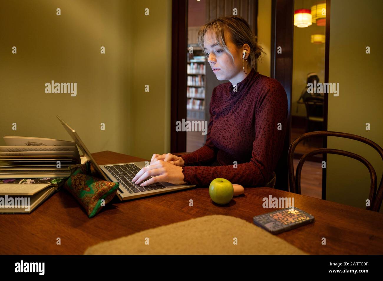 Young woman focused while working on laptop at a home study desk. Stock Photo