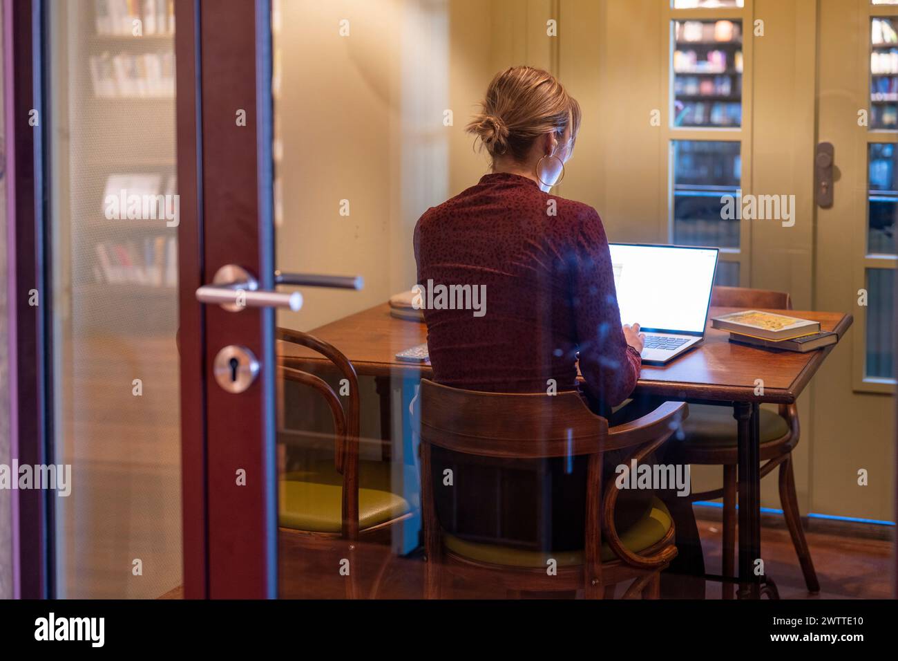 A focused individual working intently on their laptop in a cozy home library setting. Stock Photo