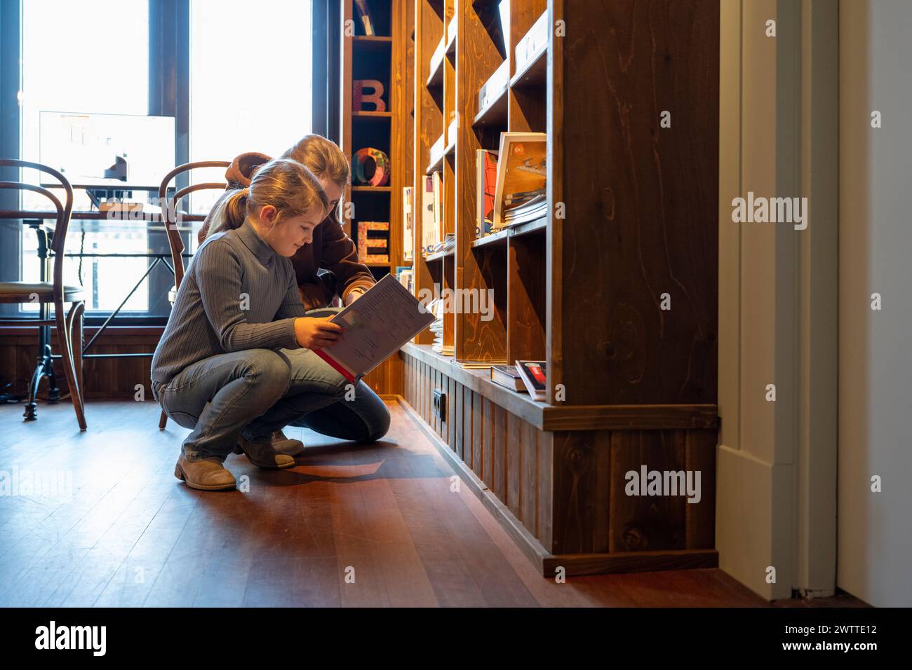 Young girl engrossed in reading a book by the bookshelf. Stock Photo