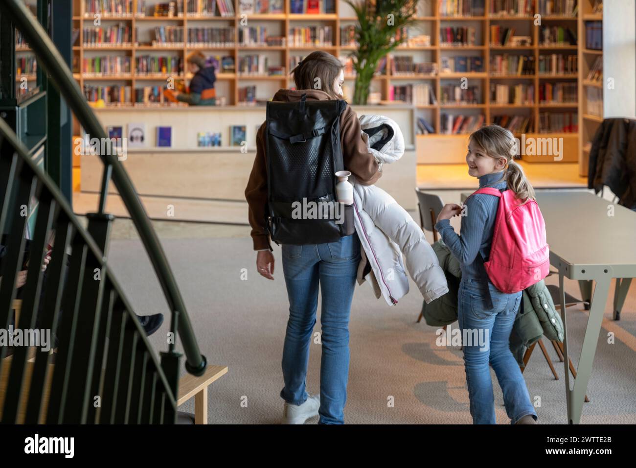 A candid moment as a woman and two children ascend the stairs in a modern library. Stock Photo