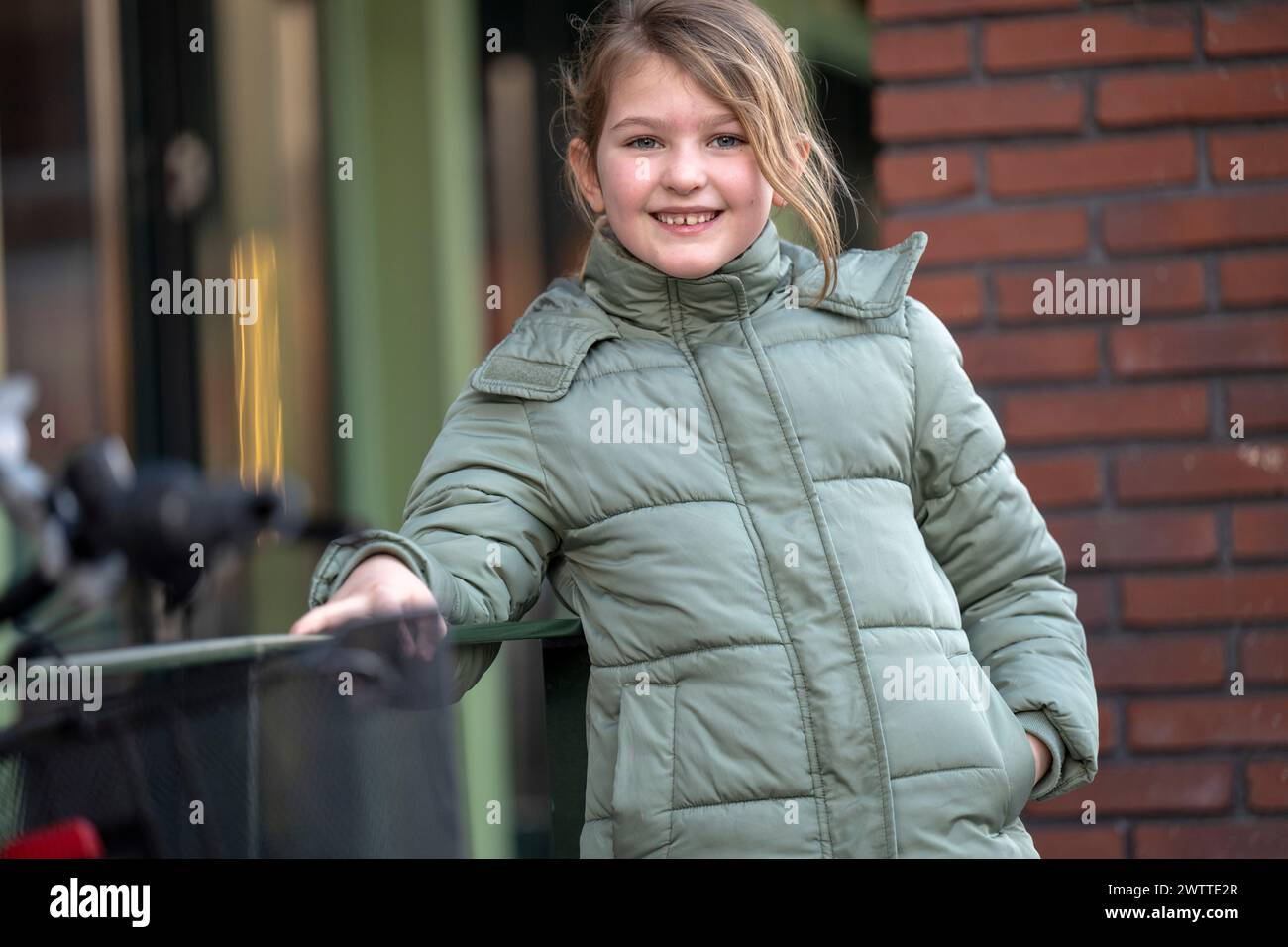 A young girl smiles warmly outdoors in a cozy green jacket Stock Photo
