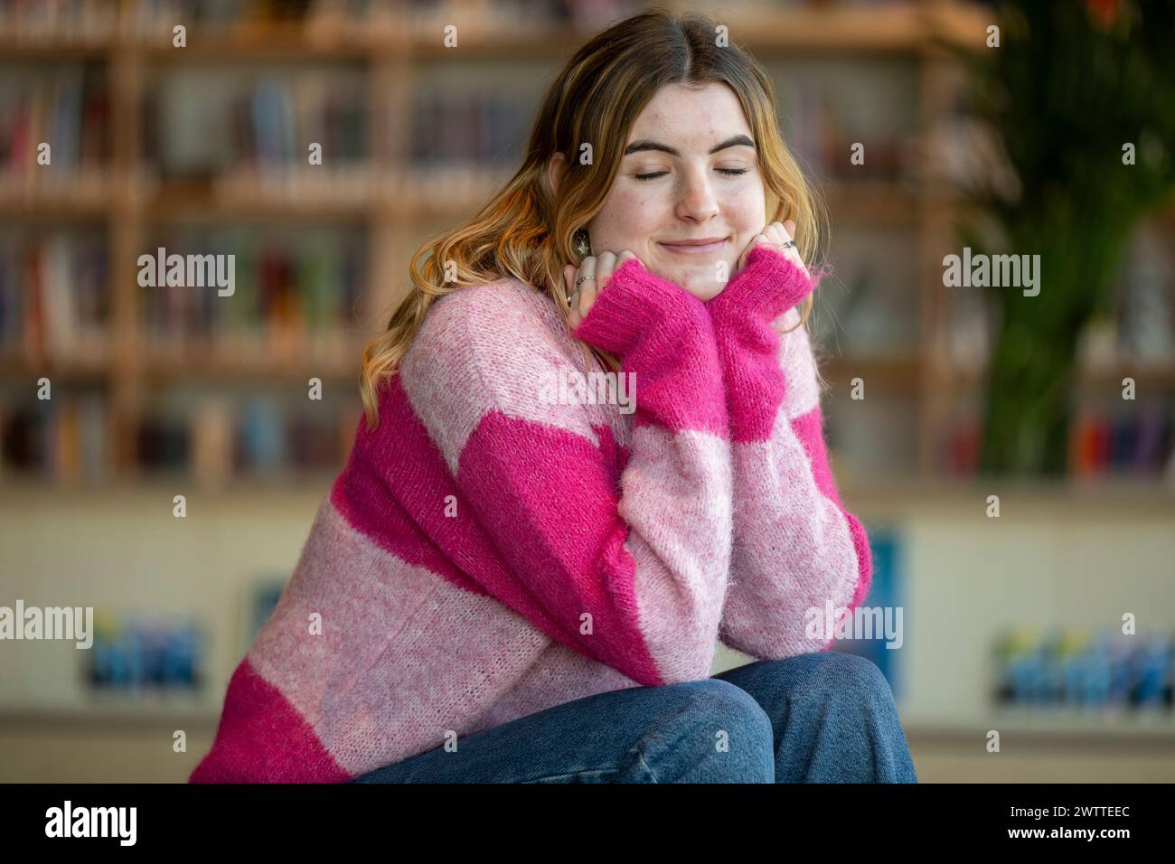 Young woman smiling and daydreaming in a cozy library setting Stock Photo