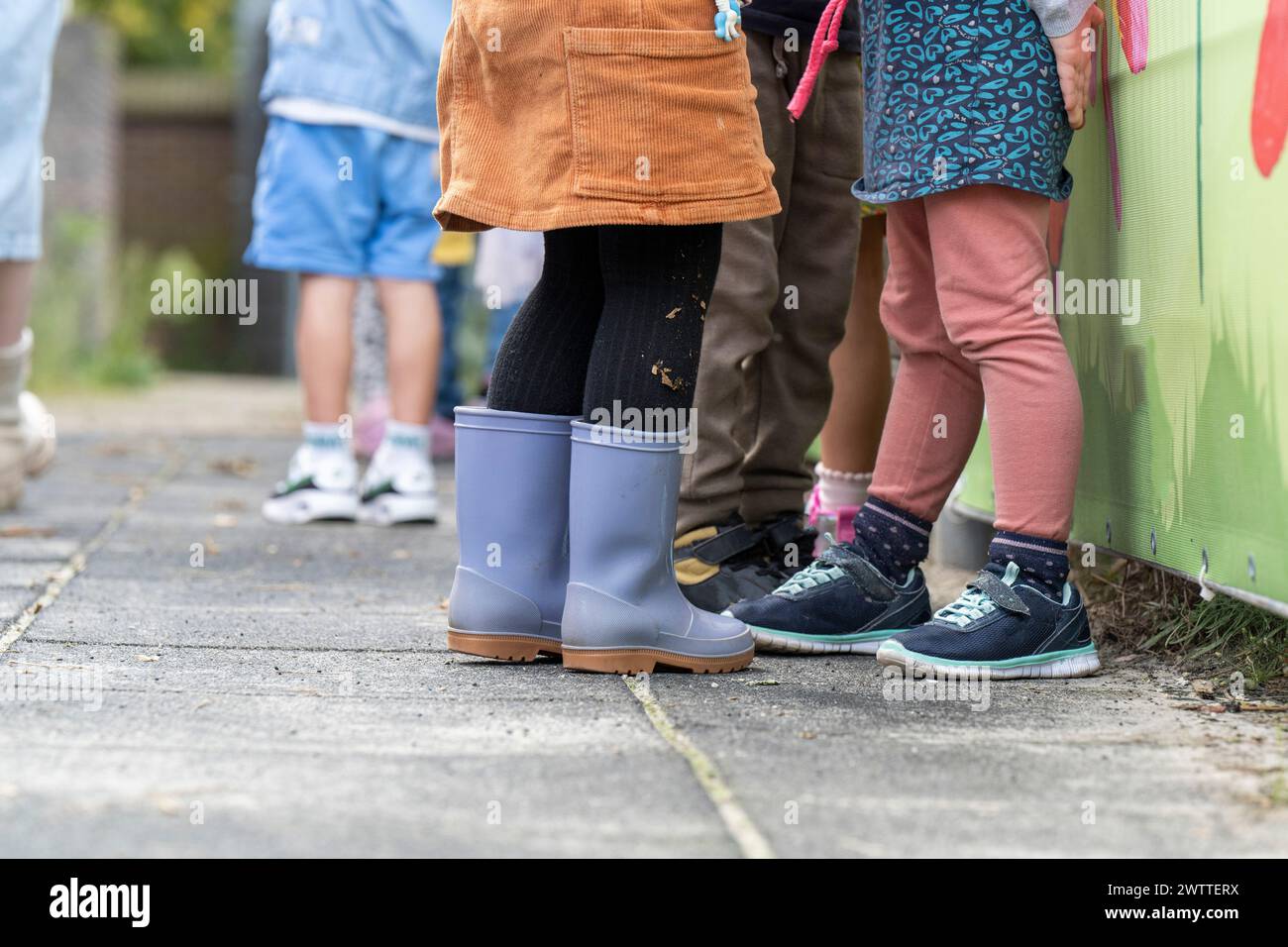 Children lined up against a colorful fence, showcasing a variety of footwear and playful attire. Stock Photo