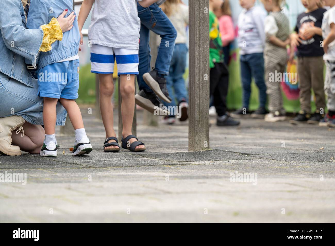 A line of diverse children captured at ground level in a park, with an adult crouching to comfort a little one. Stock Photo