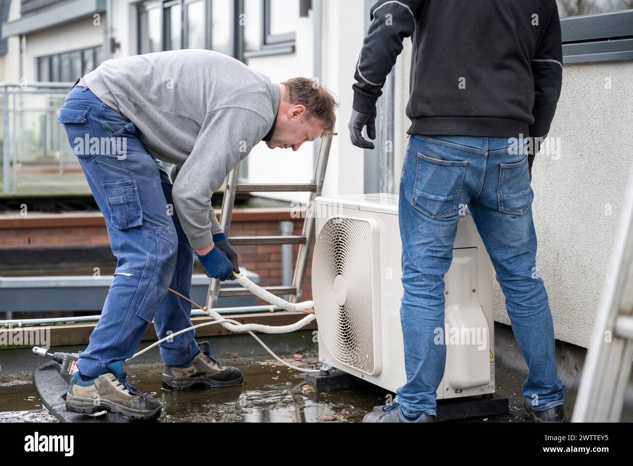 Two technicians installing an airconditioning unit outside a modern home. Stock Photo
