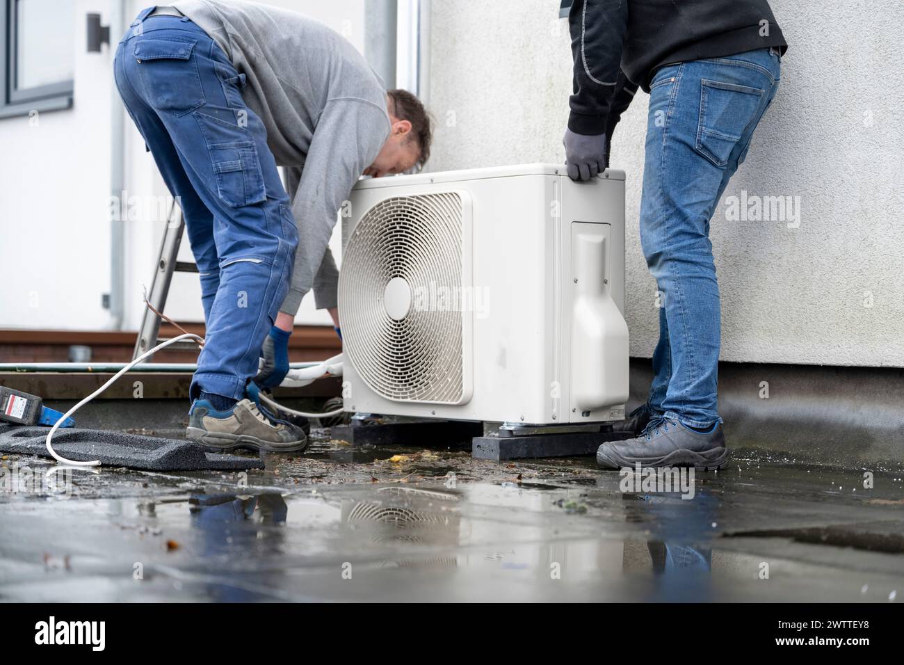 Two technicians installing an outdoor unit of a heat pump on a rooftop. Stock Photo