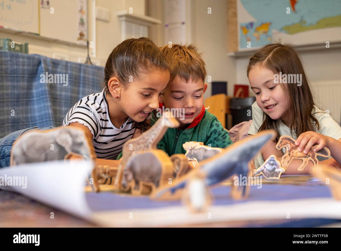 Three kids engaged and delighted, exploring a world of toy dinosaurs together. Stock Photo
