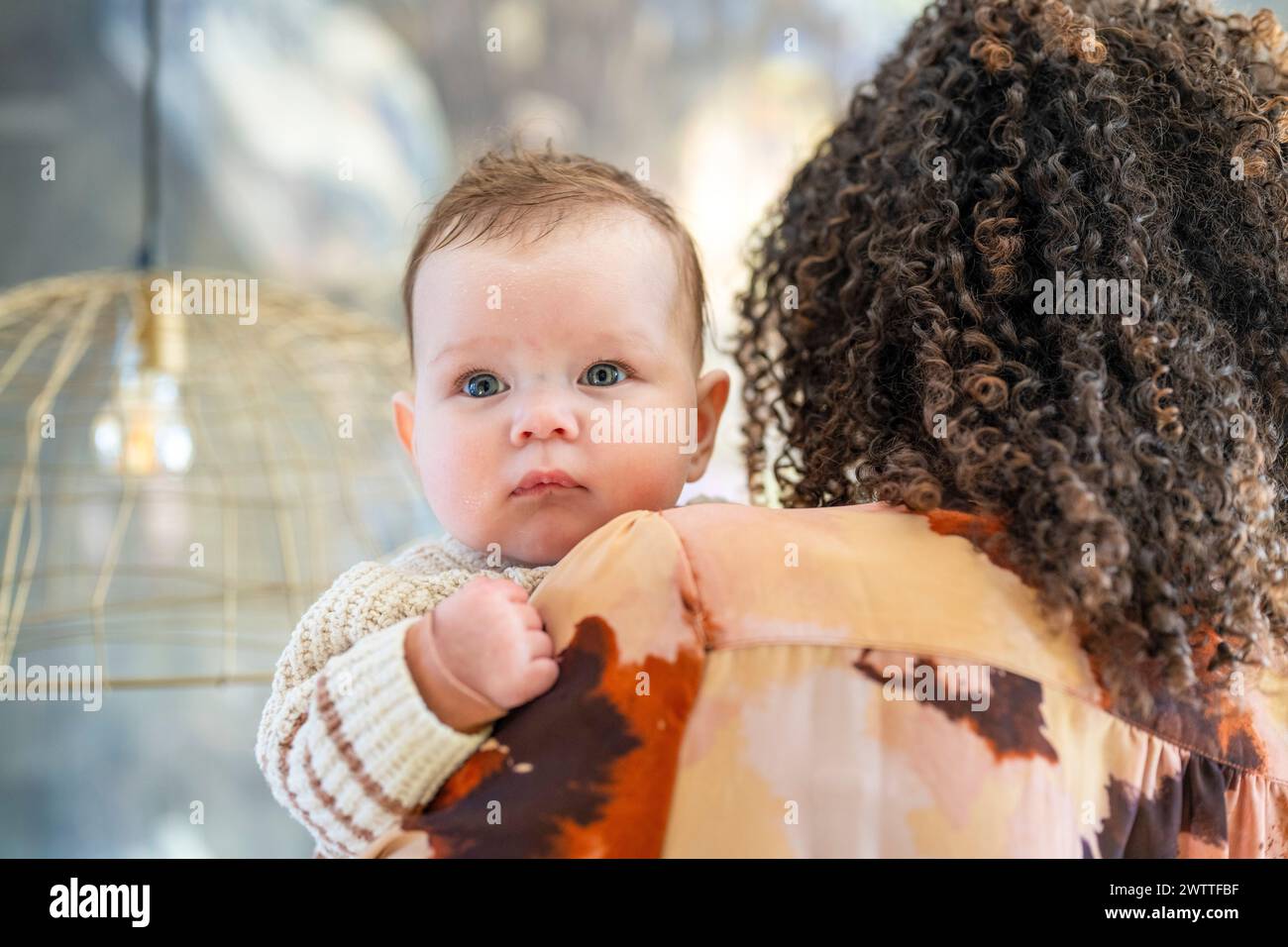 Curious baby peeking over mother's shoulder. Stock Photo