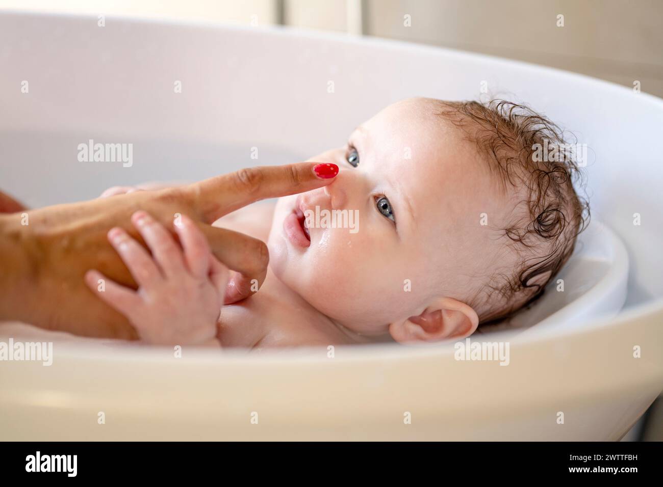 Baby's bathtime bonding moment with a playful touch on the nose Stock Photo