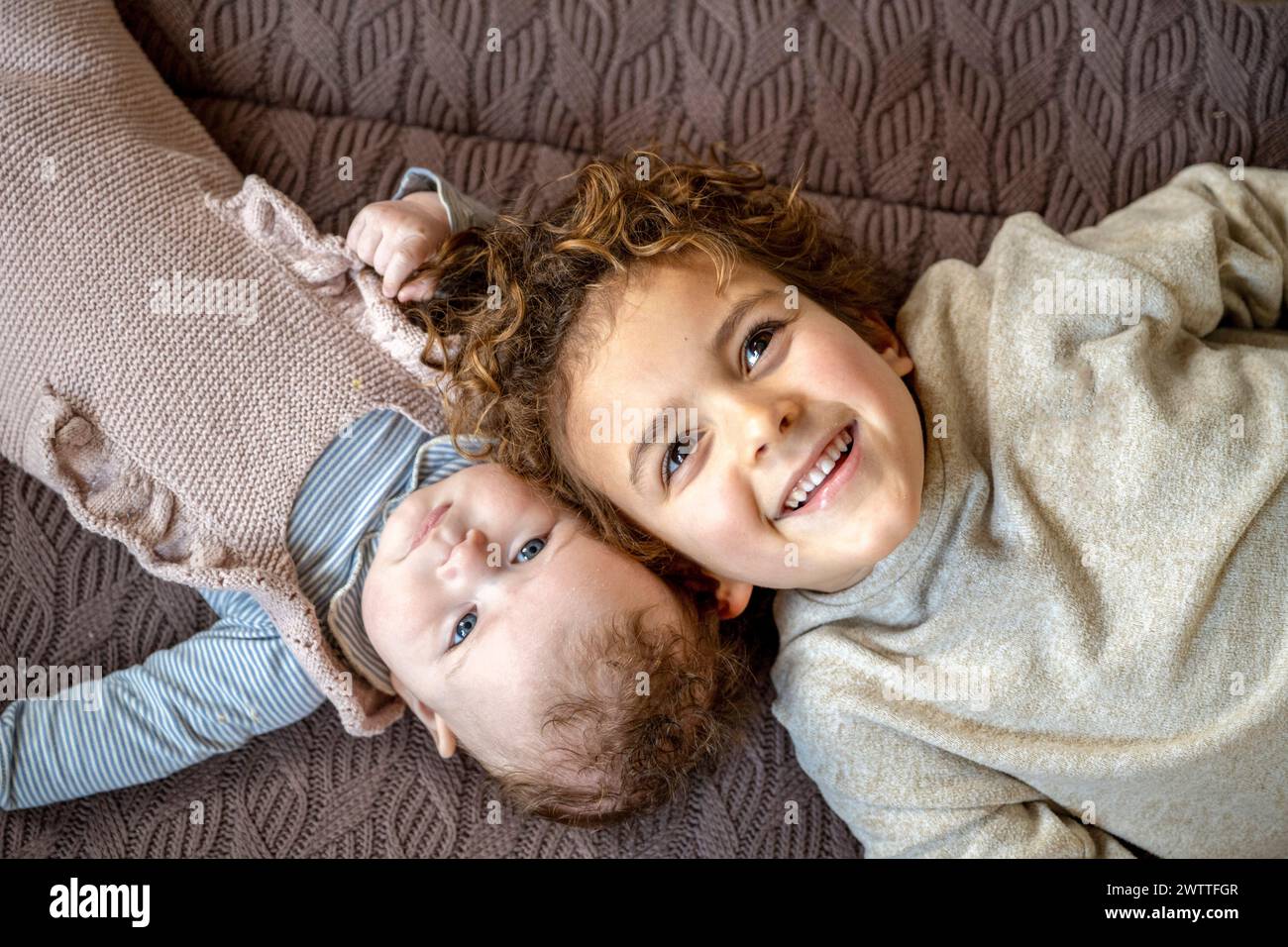 Two siblings sharing a playful moment on a cozy quilt. Stock Photo