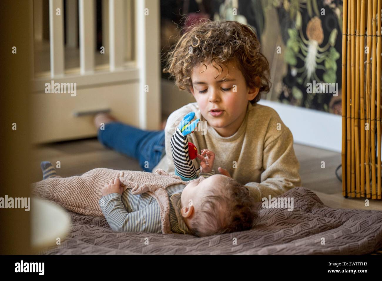 Older sibling engaging in gentle play with a baby on a cozy afternoon. Stock Photo