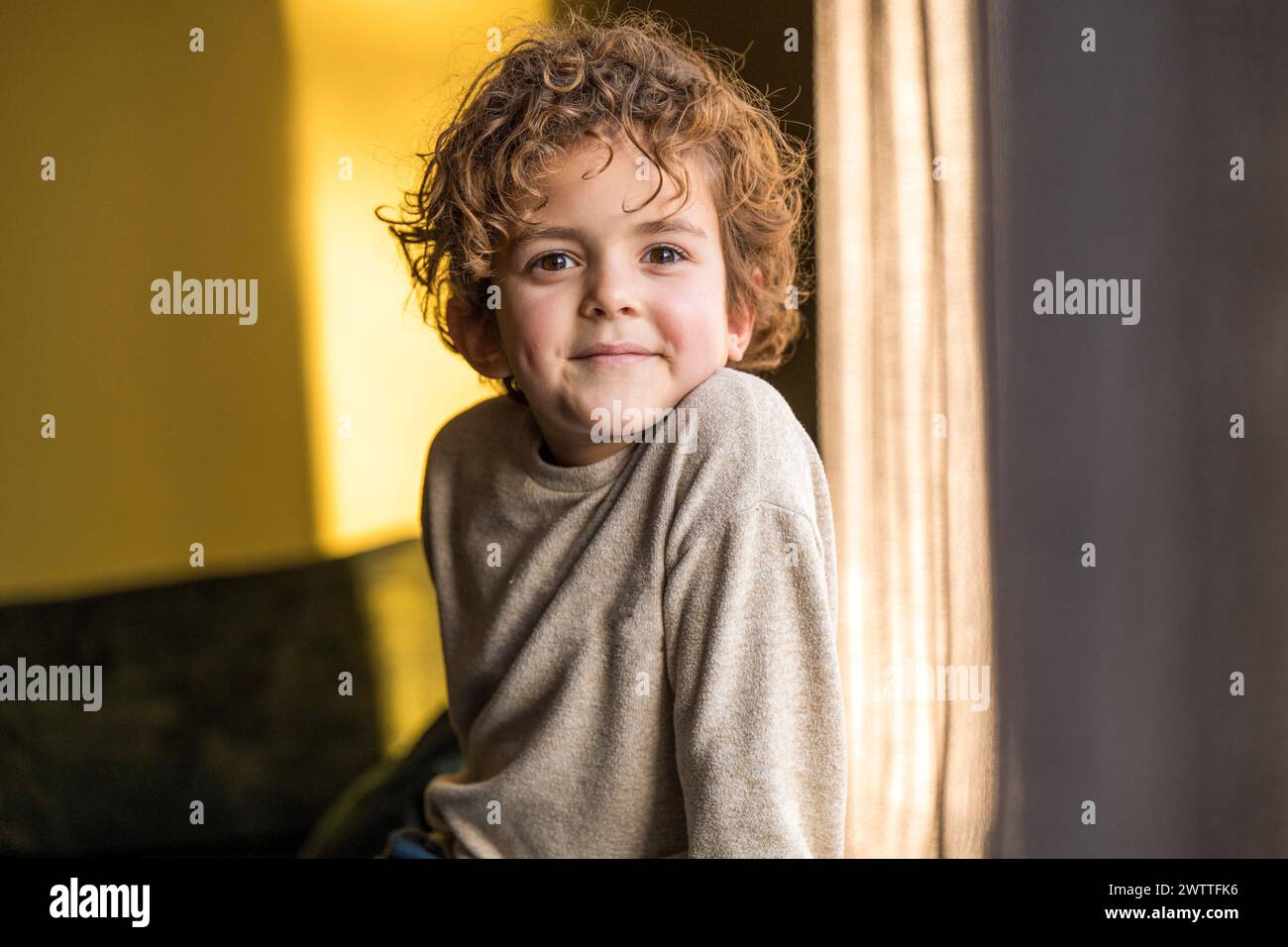 Young child with a joyful smile peeking from behind the curtains. Stock Photo