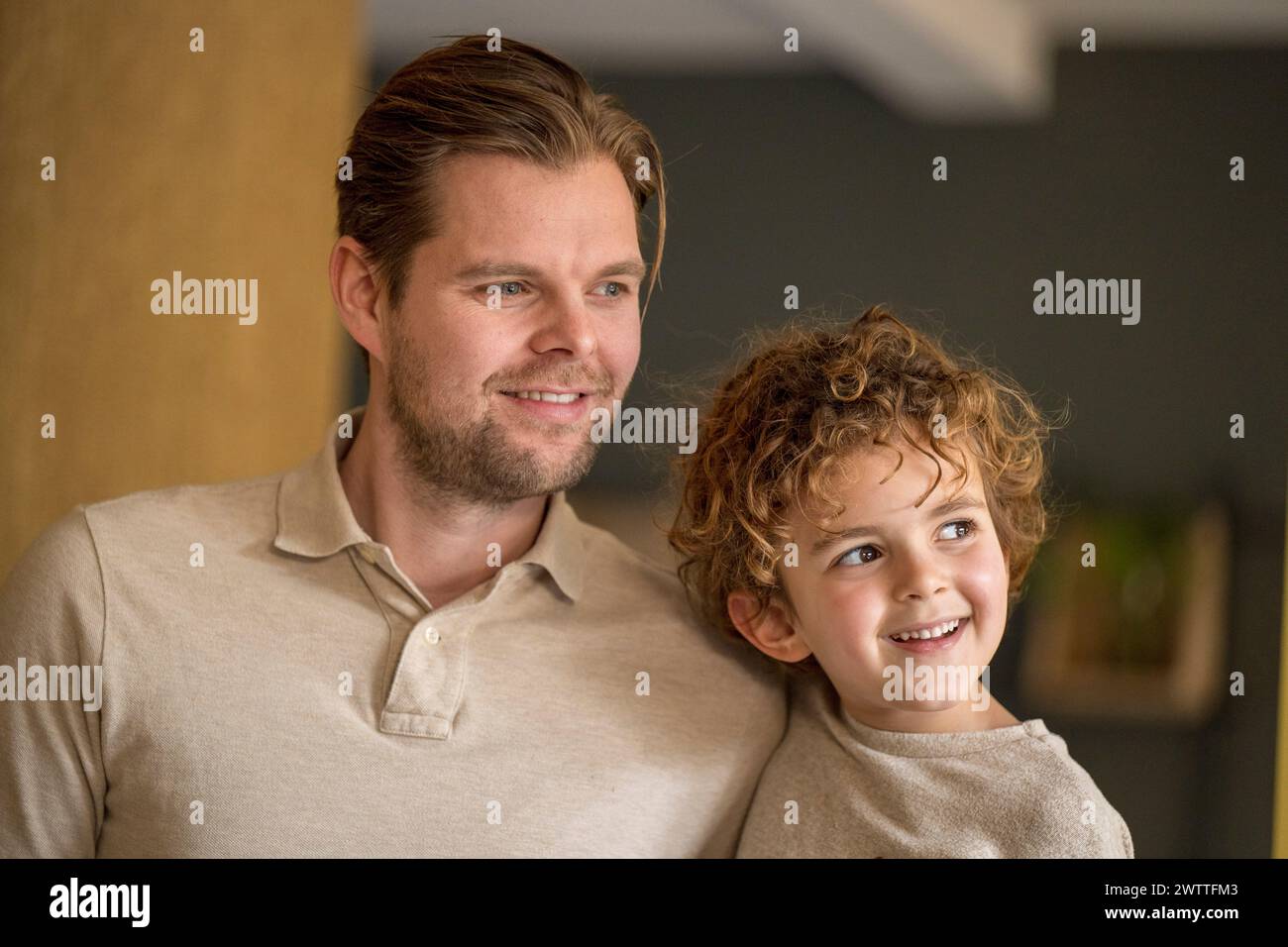 A smiling young child looks to the side with admiration beside a content adult male indoors Stock Photo