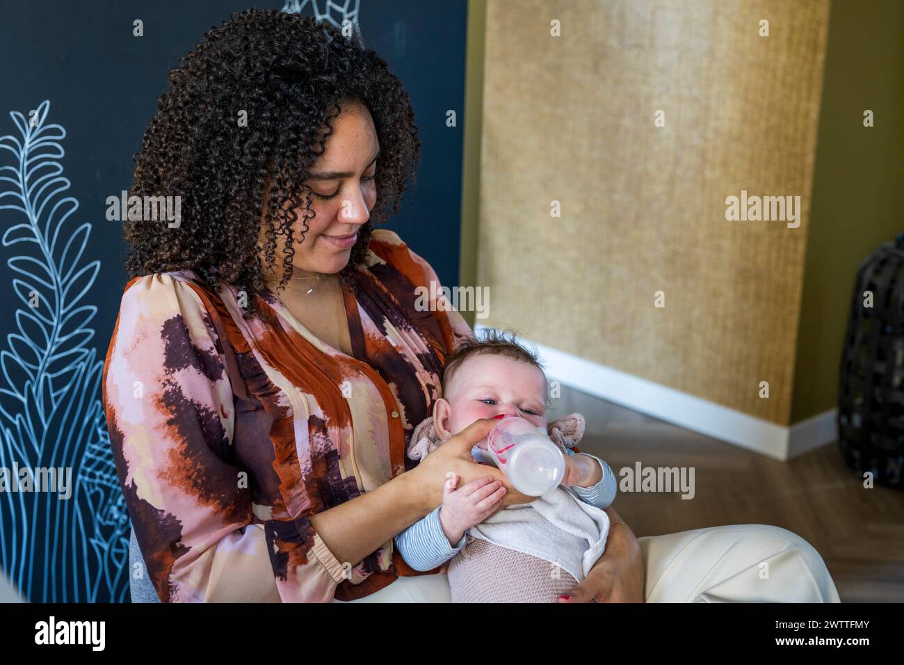 A mother tenderly feeds her baby with a bottle. Stock Photo