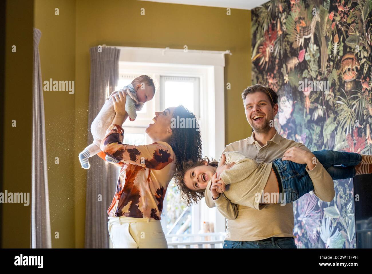 Family fun time as a parent lifts a joyful child into the air in a cozy home setting. Stock Photo